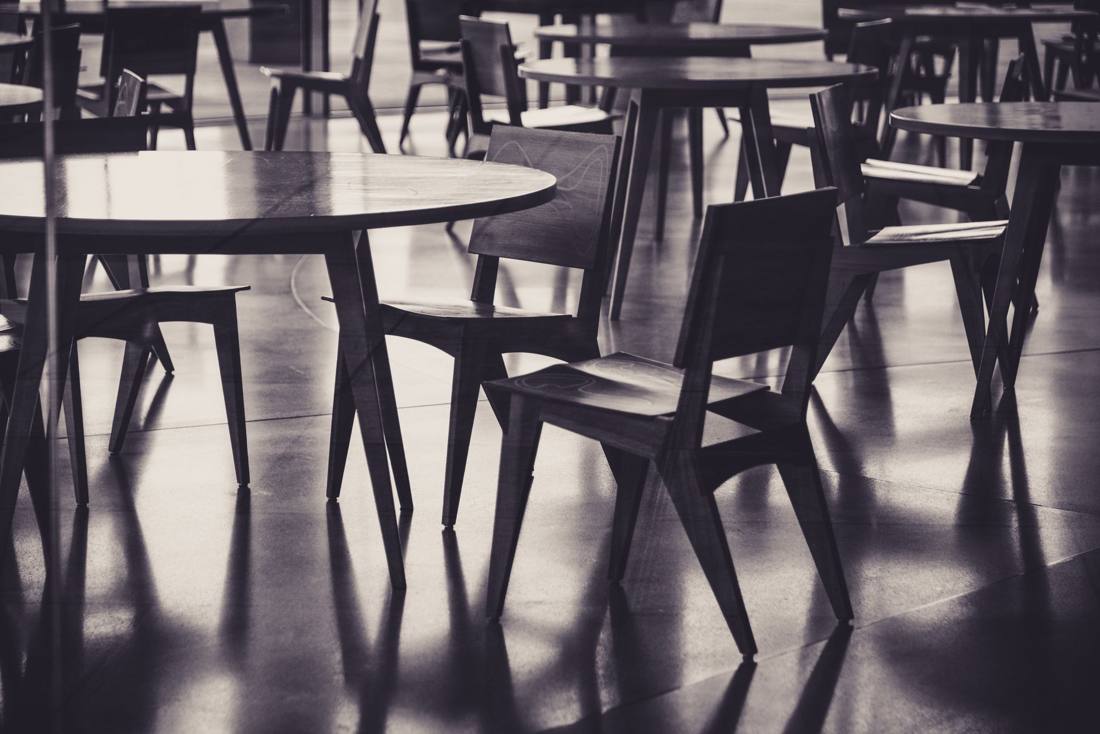 A black and white abstract photo of empty wooden chairs and tables in a cafe setting.