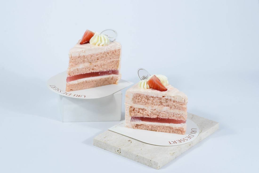 Close-up of two slices of pink layered cake with strawberry garnish on white background. Perfect for dessert themed presentations.