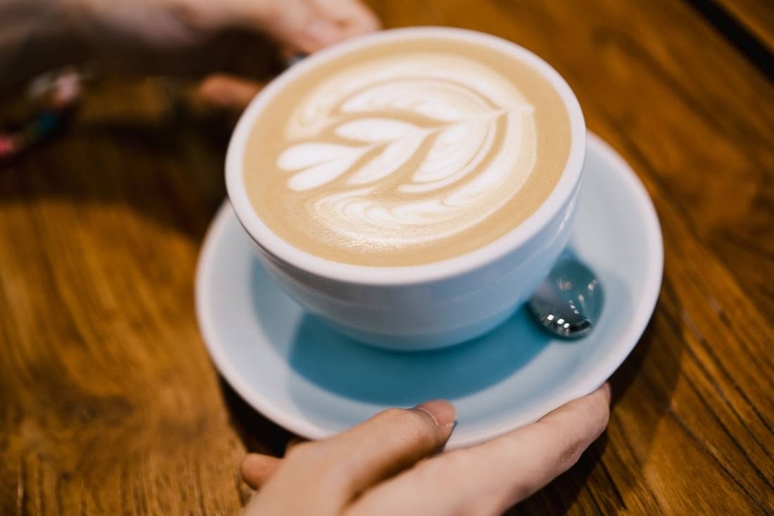 A detailed view of a latte with elegant art in a white cup on a wooden table.